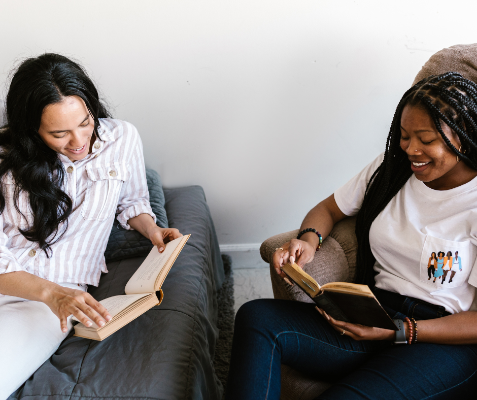 2 Frauen sitzen sich gegenüber, jede hält ein Buch in der Hand. Beide lächeln, als würden sie sich über die Bücher unterhalten