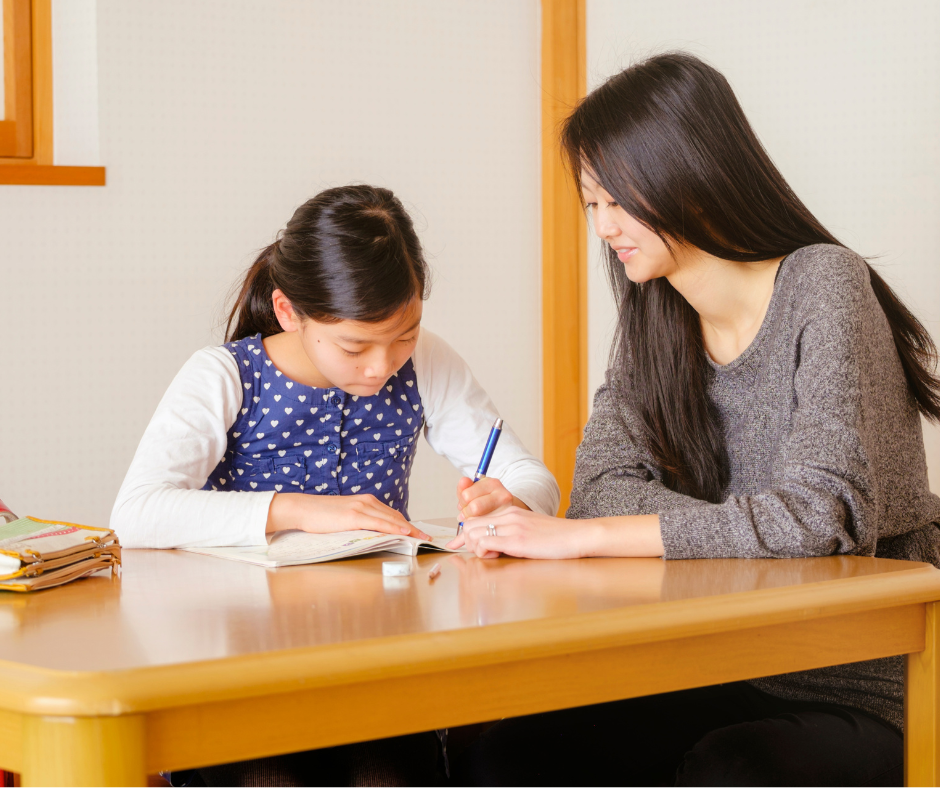 Eine Frau sitzt mit einer Schülerin am Tisch beim Lernen