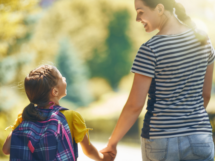 Schulkind und Frau laufen Hand in Hand